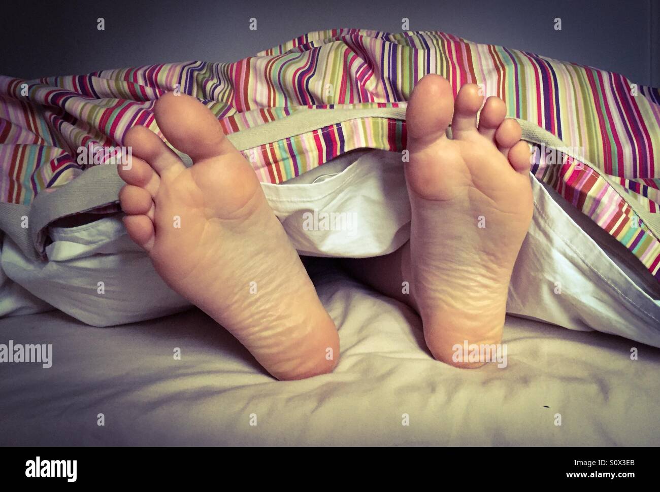 Wakey Wakey! Piedi prendendo fuori da sotto il piumone - Immagine stock catturata con smartphone