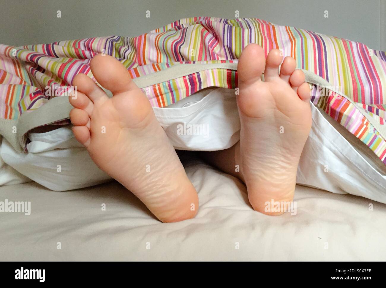 Wakey Wakey! Piedi prendendo fuori da sotto il piumone - Immagine stock catturata con smartphone