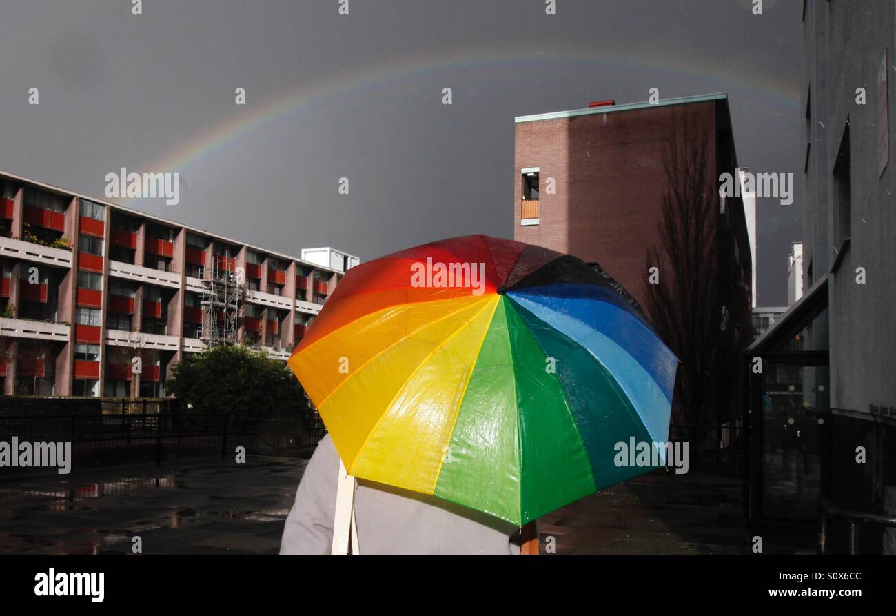 Una donna porta un ombrello come lei cammina attraverso un consiglio station wagon e un arcobaleno nella zona est di Londra Foto Stock