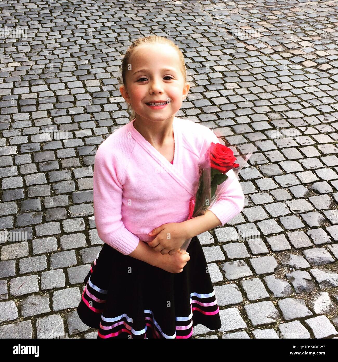 Una giovane ragazza pone con una rosa rossa dopo aver tenuto il suo grado 1 esame di balletto presso la Reale Accademia di danza a Londra Foto Stock