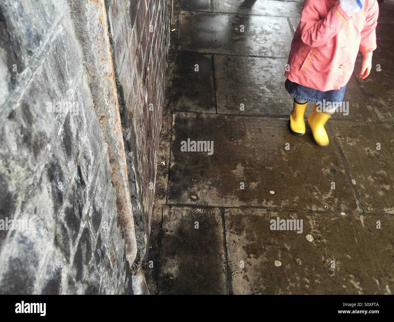 Bambino a piedi da un indossato un muro di mattoni Foto Stock