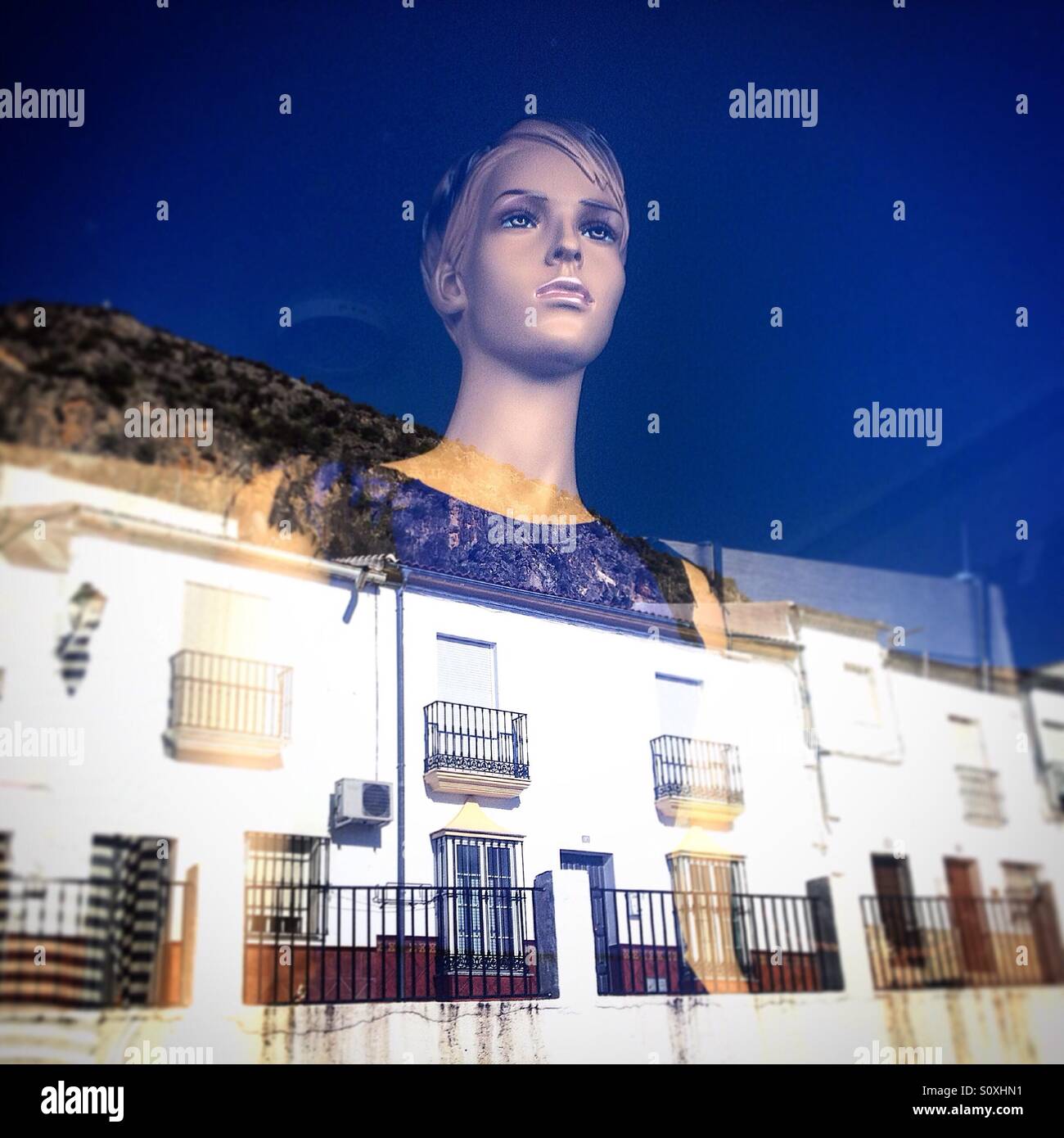 La testa di un manichino è riflessa nella vetrina di un negozio in una strada a Algodonales, Sierra de Cadice, Andalusia, Spagna Foto Stock