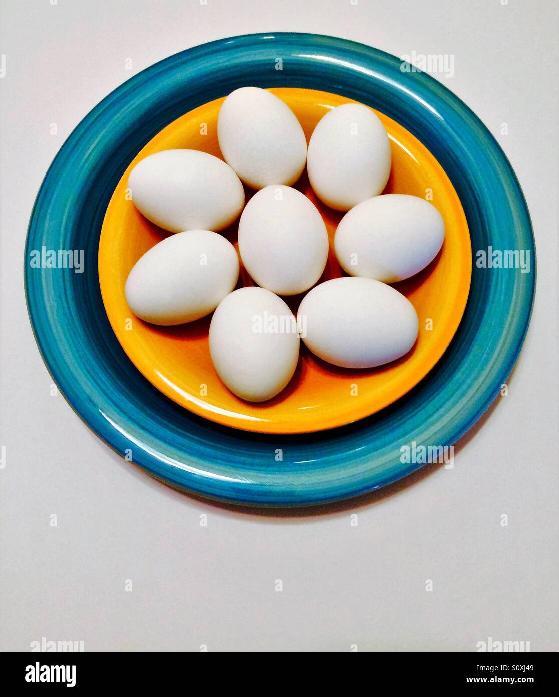 Tutta le uova bianche in giallo e blu ciotola vista aerea su sfondo bianco - Immagine stock catturata con smartphone