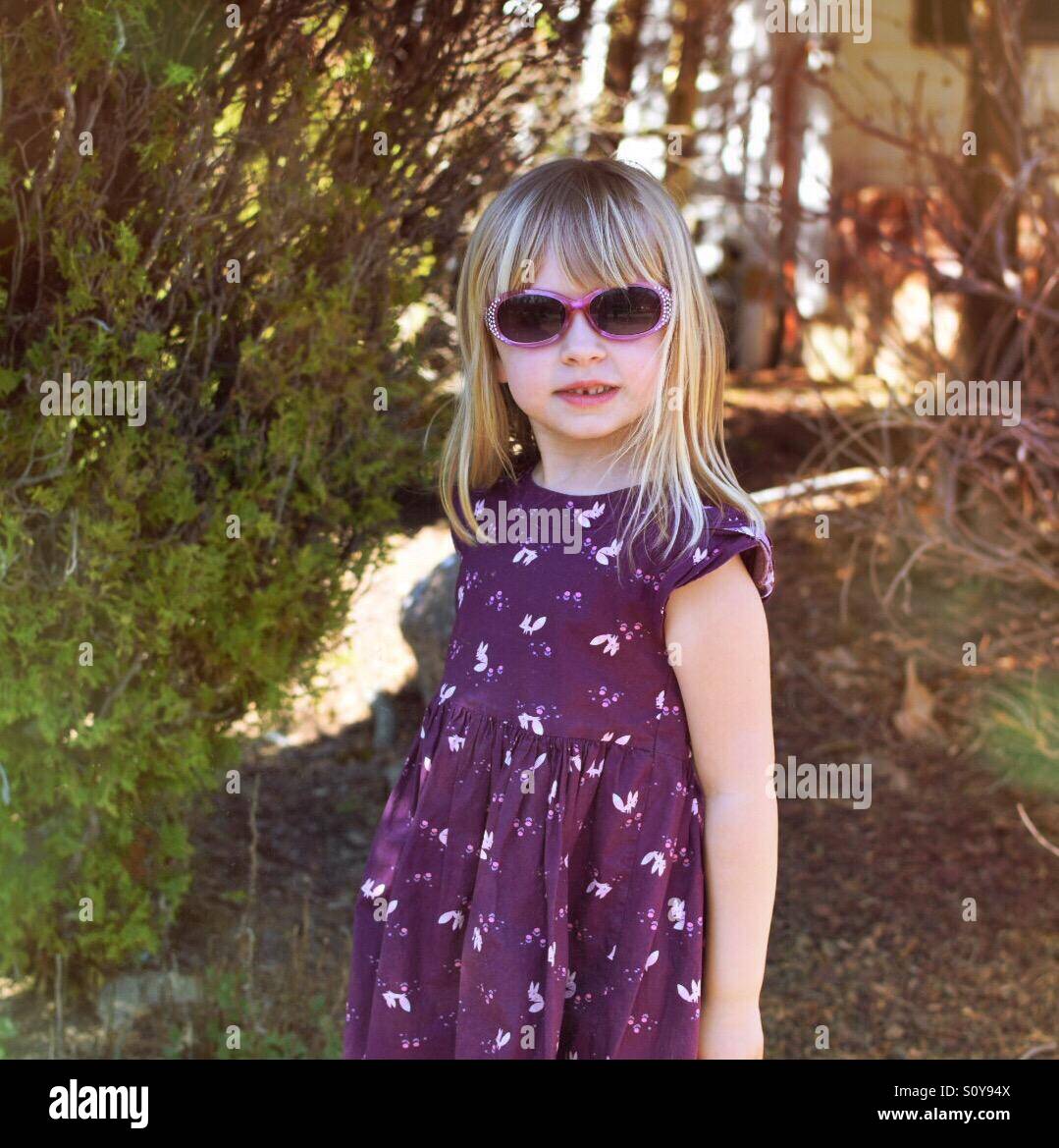 Ragazza giovane la modellazione di occhiali da sole e vestito viola all'aperto Foto Stock