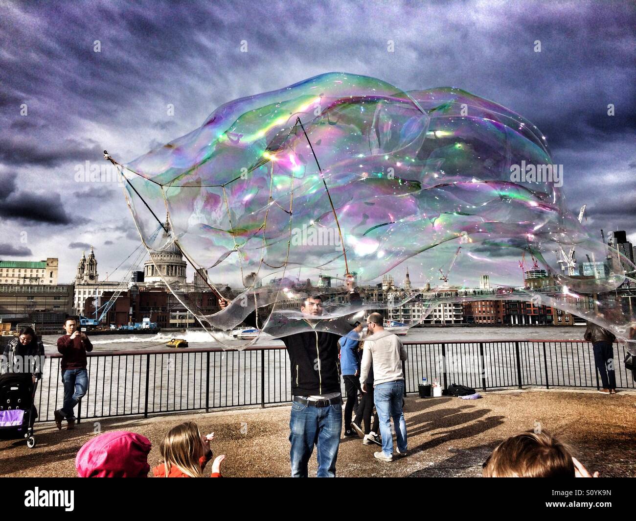 Busker intrattiene la folla sulla South Bank di Londra tramite soffiaggio di enormi bolle di sapone. La Cattedrale di St Paul e può essere visto in background Foto Stock