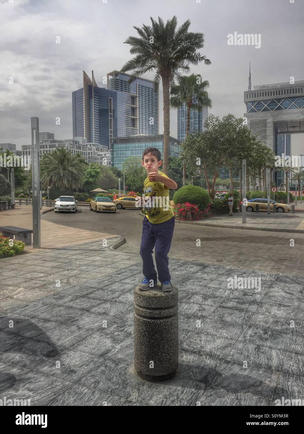 Felice ragazzo pollice alzato in piedi su un bollard su una strada a Dubai Foto Stock