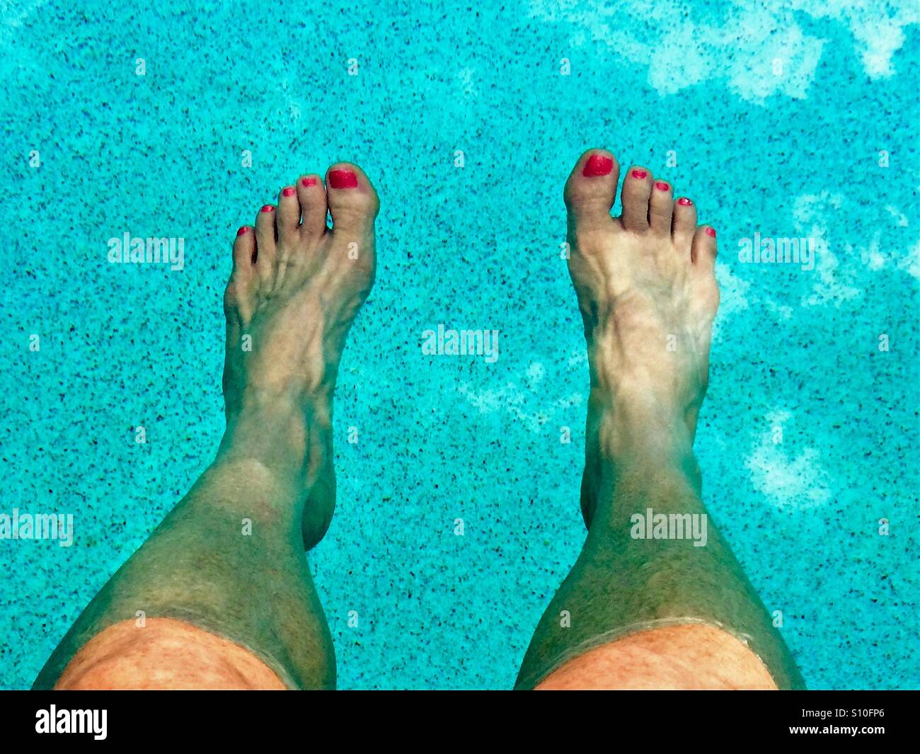 Donna con puntale rosso smalto per unghie il raffreddamento le sue gambe presso la piscina del bordo - Immagine stock catturata con smartphone