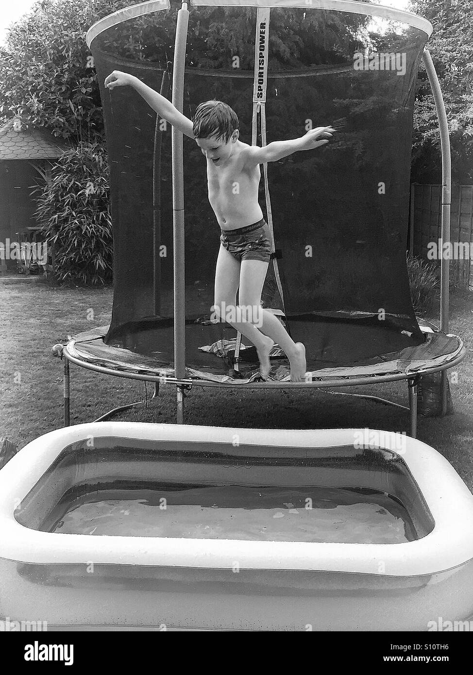 Ragazzo giovane salto in una piscinetta per bambini Foto Stock