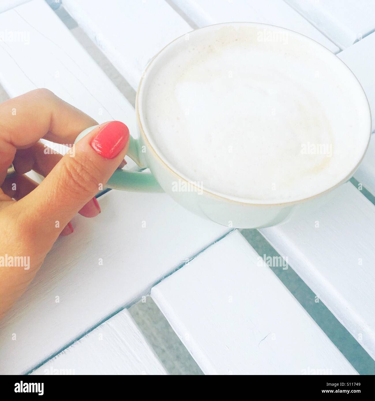 Donna di mano sinistra tenendo premuto su una tazza di caldo cappuccino schiumoso. - Immagine stock catturata con smartphone
