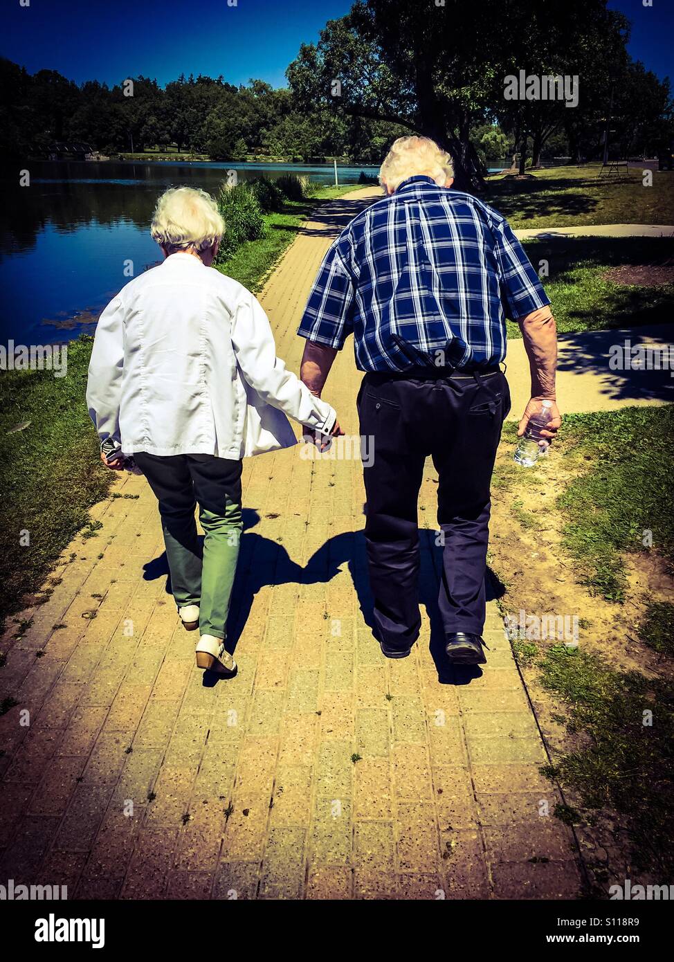 Coppia molto vecchia, ancora insieme dopo decenni. Forse l'ultima tappa del loro viaggio. Fuori sulla loro passeggiata quotidiana vicino al fiume, Ontario, Canada. Due Stati Uniti. Io e te. - Immagine stock catturata con smartphone