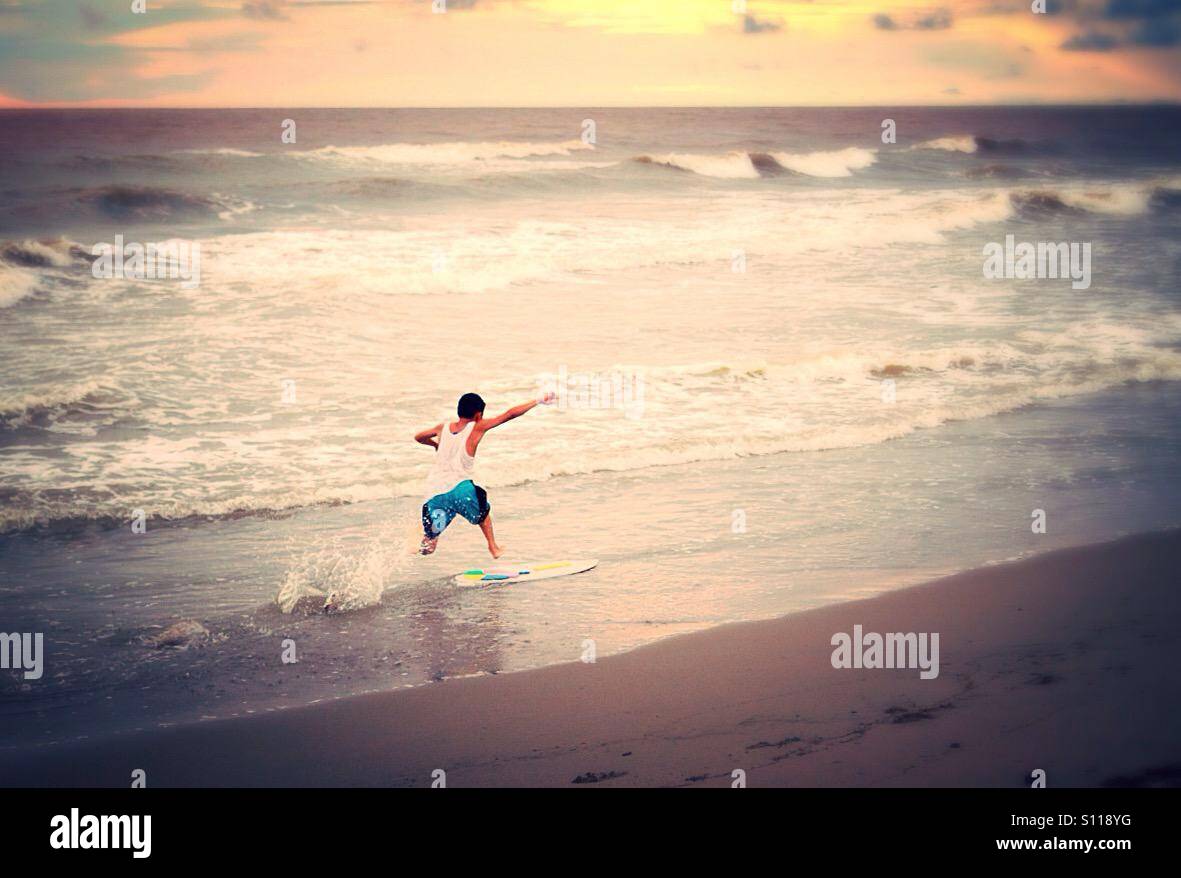 Ragazzo e la sua tavola da surf al tramonto Foto Stock