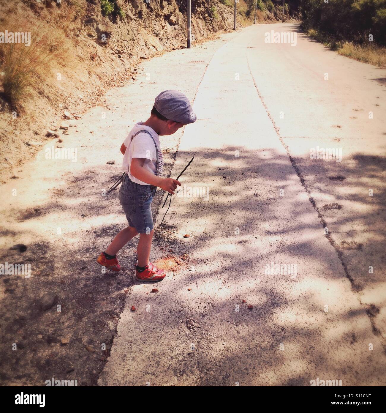 Il capretto con un bastone in mano nel mezzo di una strada di campagna Foto Stock