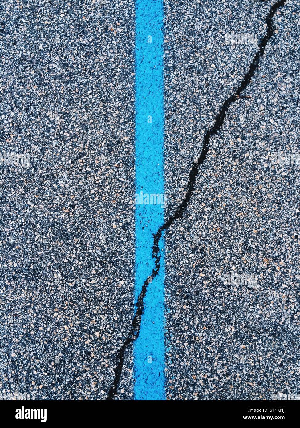 Un dipinto di blu linea in un parcheggio con una crepa in asfalto che corre attraverso di esso. Foto Stock