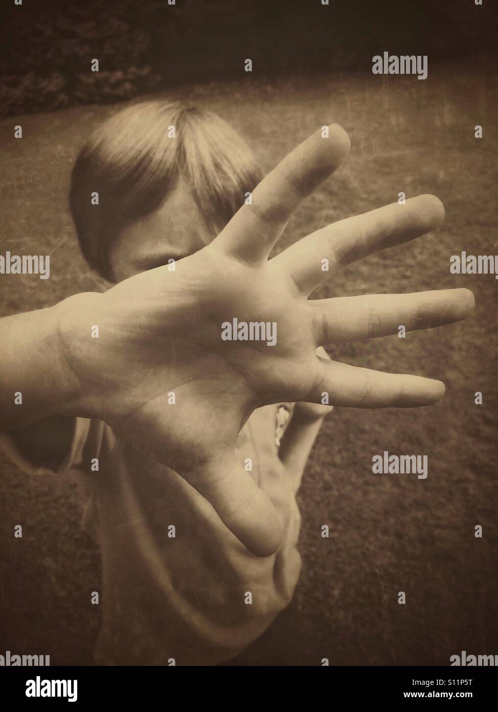 Un bambino di sei anni ragazzo si copre il viso stendendo le sue dita e spingendo la sua mano verso la telecamera. Un'immagine per illustrare il bambino le questioni sociali. Credito foto - © COLIN HOSKINS. - Immagine stock catturata con smartphone