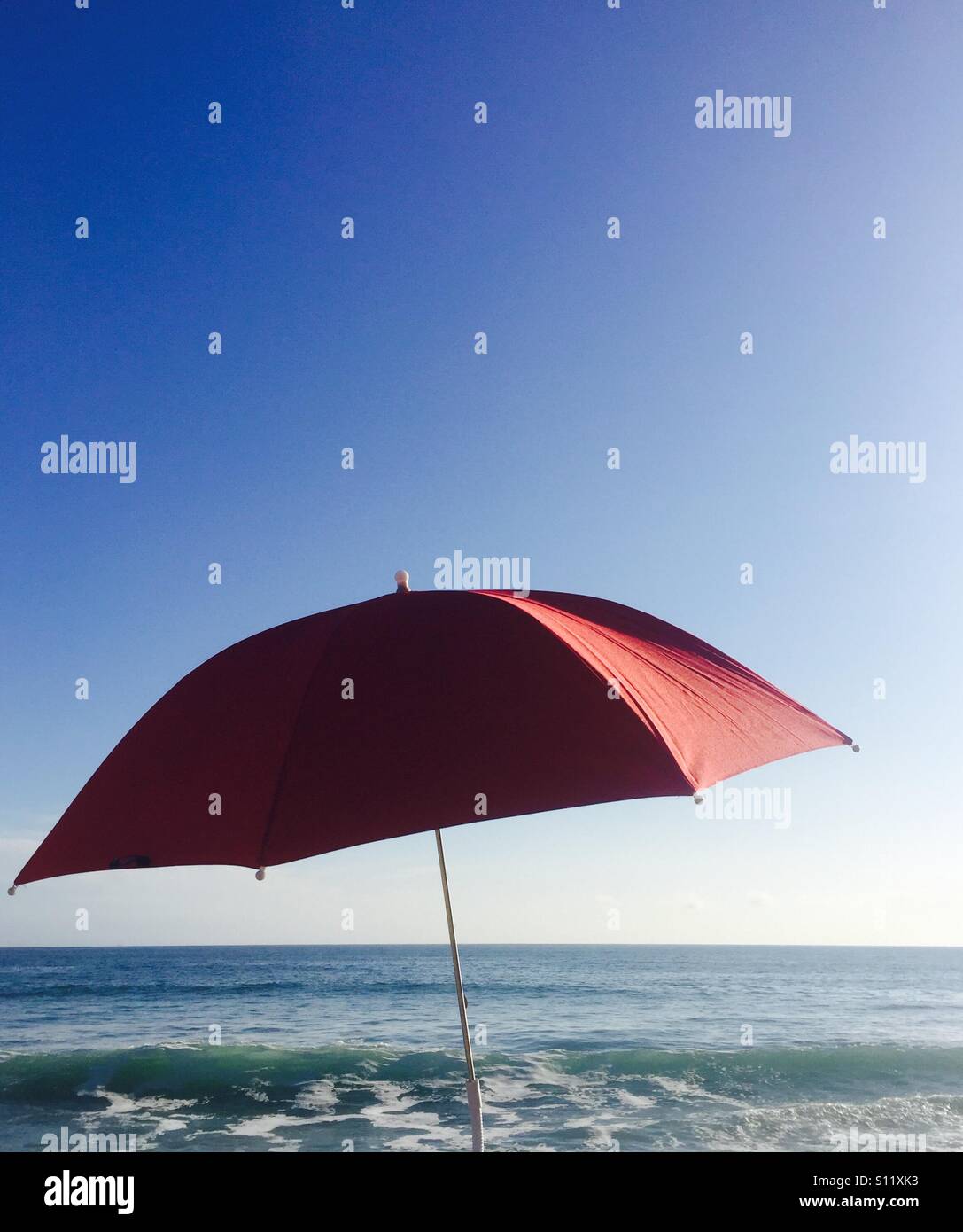 Un unico ombrello rosso e l'oceano e cielo. Ventura, California USA. Foto Stock