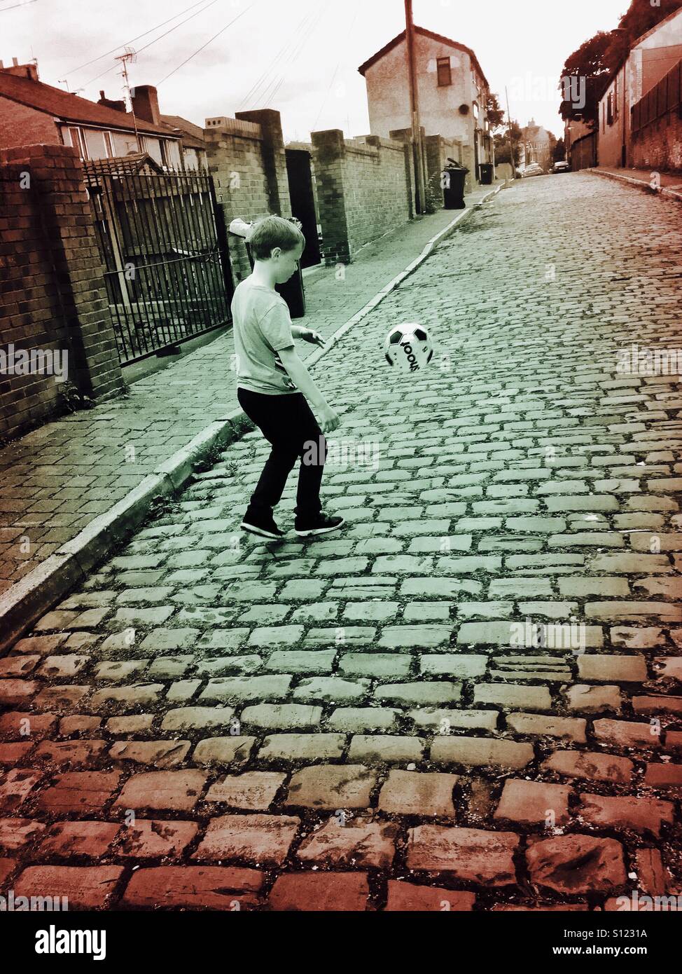 Ragazzo giocando a calcio per strada. Foto Stock