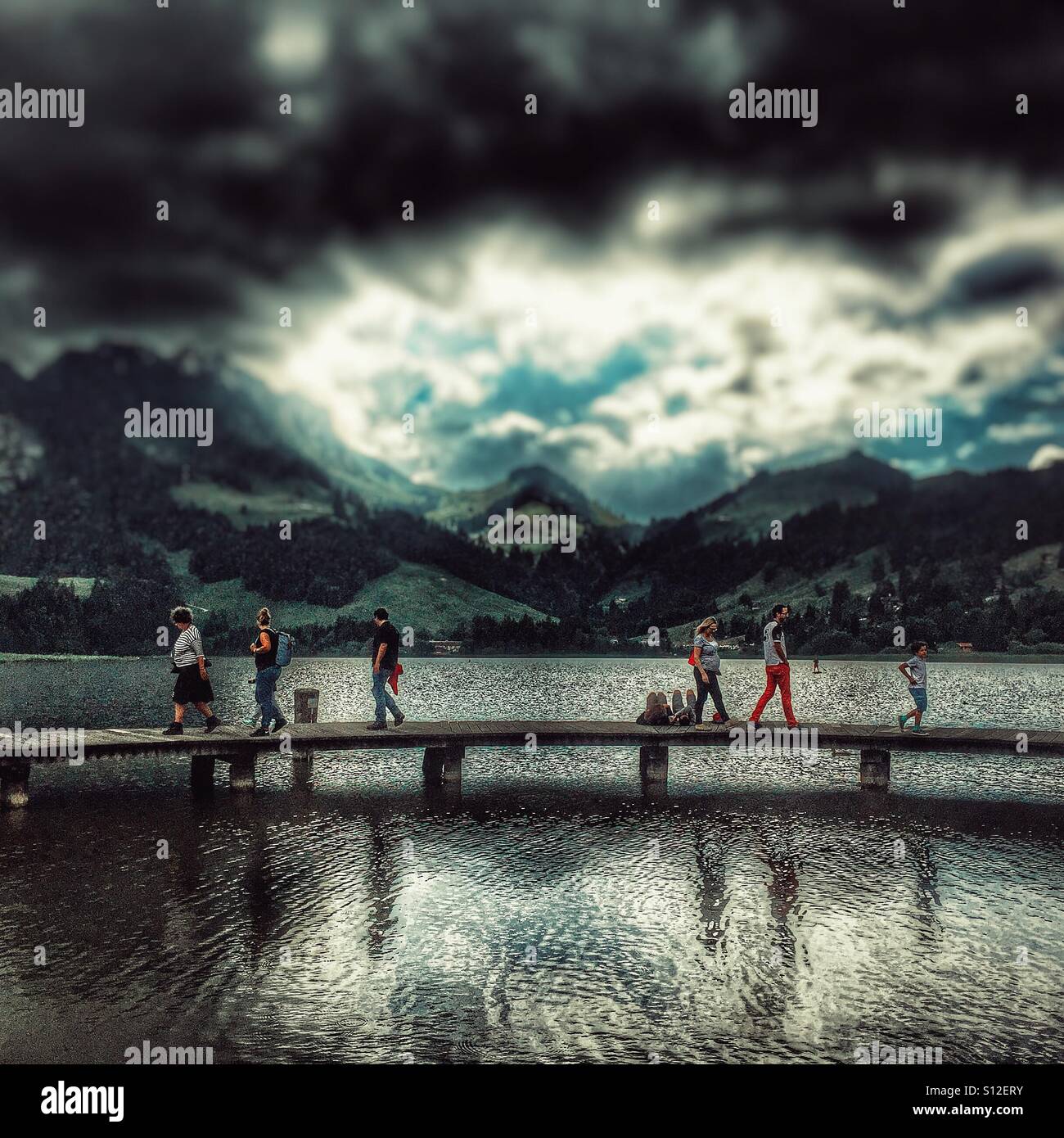 Le figure a camminare su una passerella accanto a un lago svizzero, come il cielo minaccia pioggia Foto Stock
