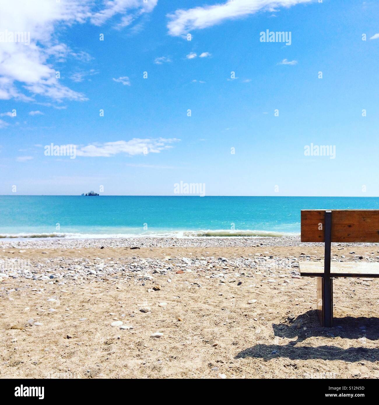 Banco solitario su una spiaggia spagnola in fronte al mare Mediterraneo in una limpida giornata di primavera - Immagine stock catturata con smartphone