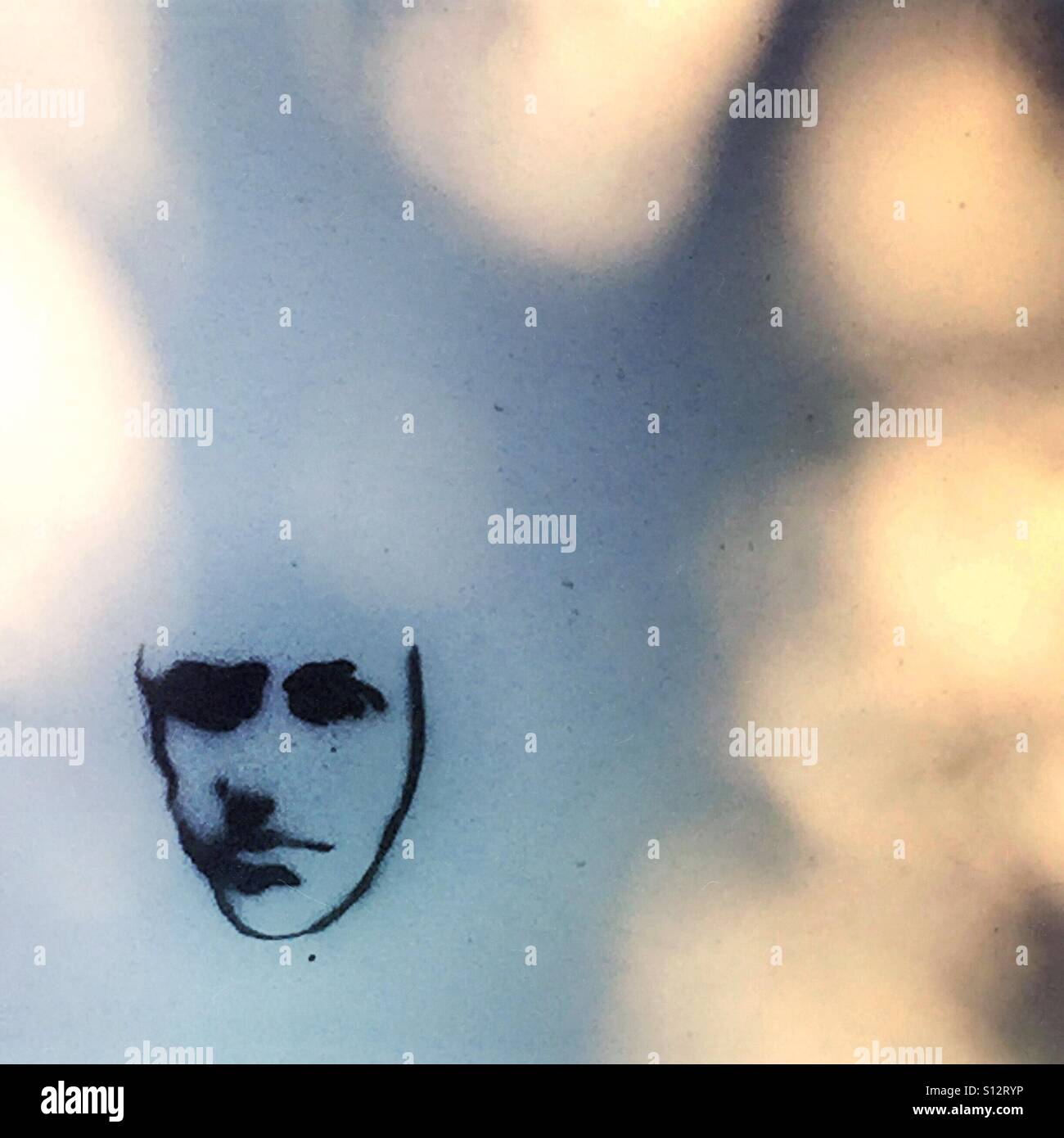 Il volto triste e graffiti su una parete con l'ombra di un albero Foto Stock