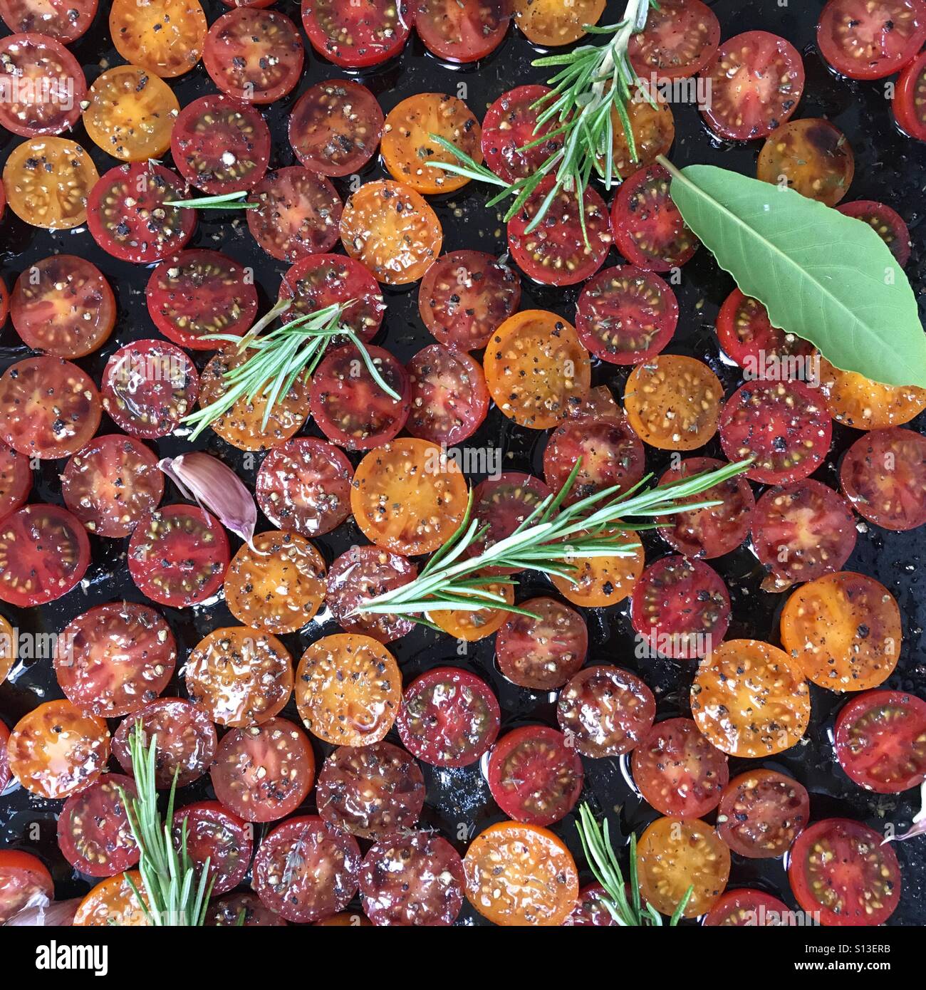 Condito in rosso e arancione pomodorini con il rosmarino e la foglia di alloro erbe Foto Stock