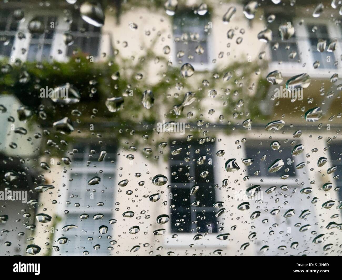 Le gocce di pioggia sul parabrezza guardando edificio con vite rampicante - Immagine stock catturata con smartphone