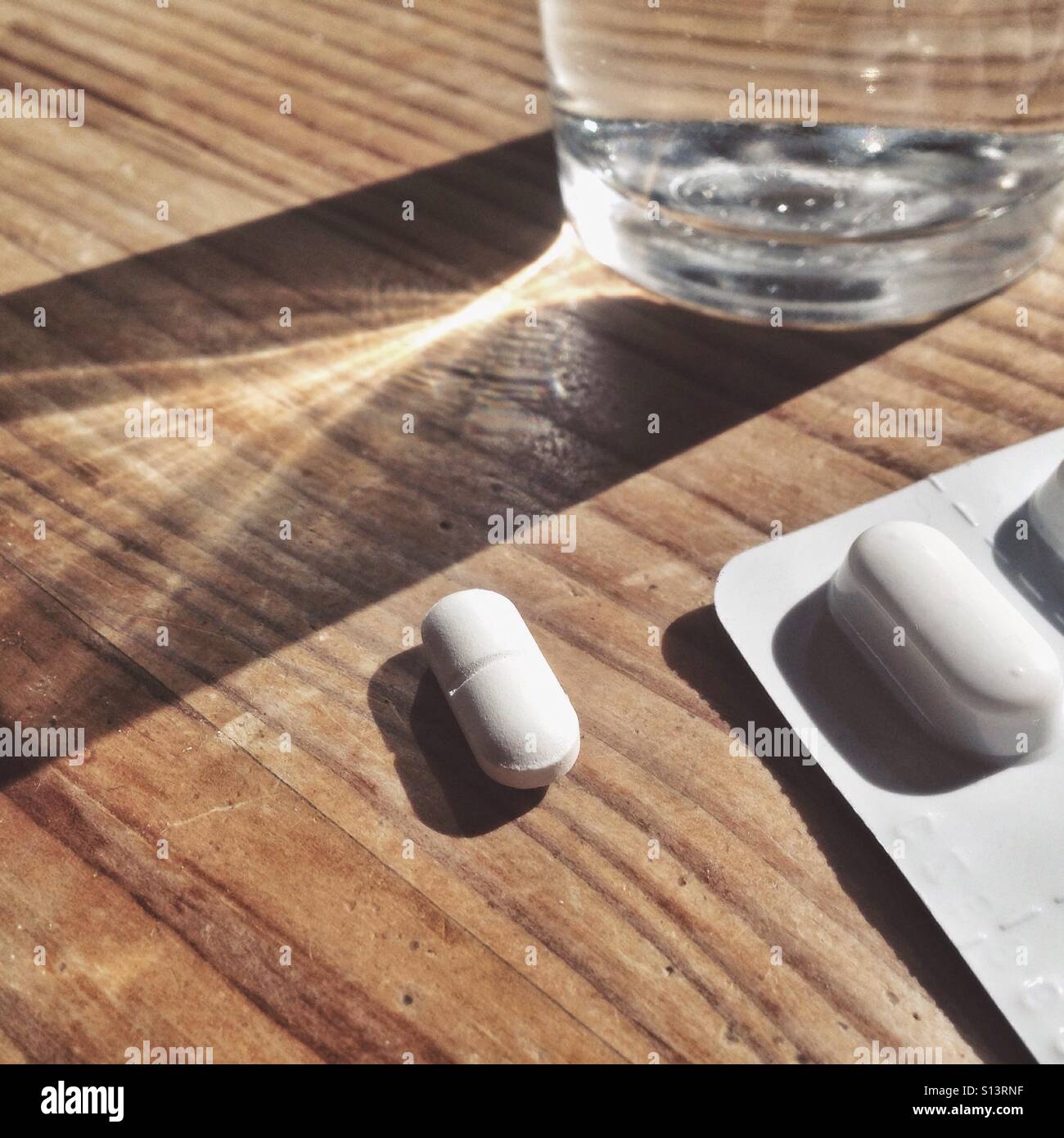 Antidolorifico pillola, blister e il bicchiere di acqua su una superficie in legno Foto Stock