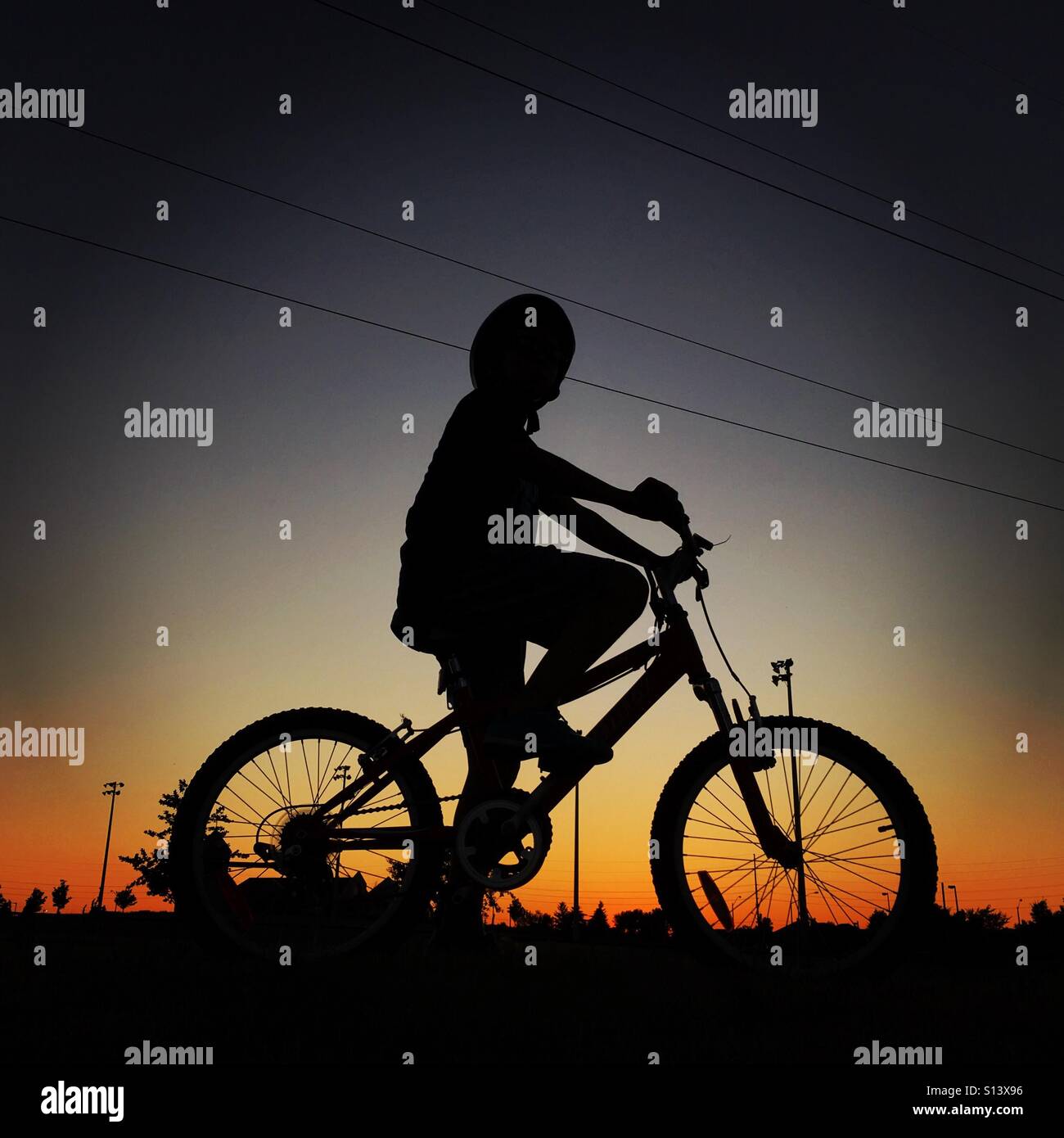 Un ragazzo in sella alla sua moto nel parco al tramonto Foto Stock