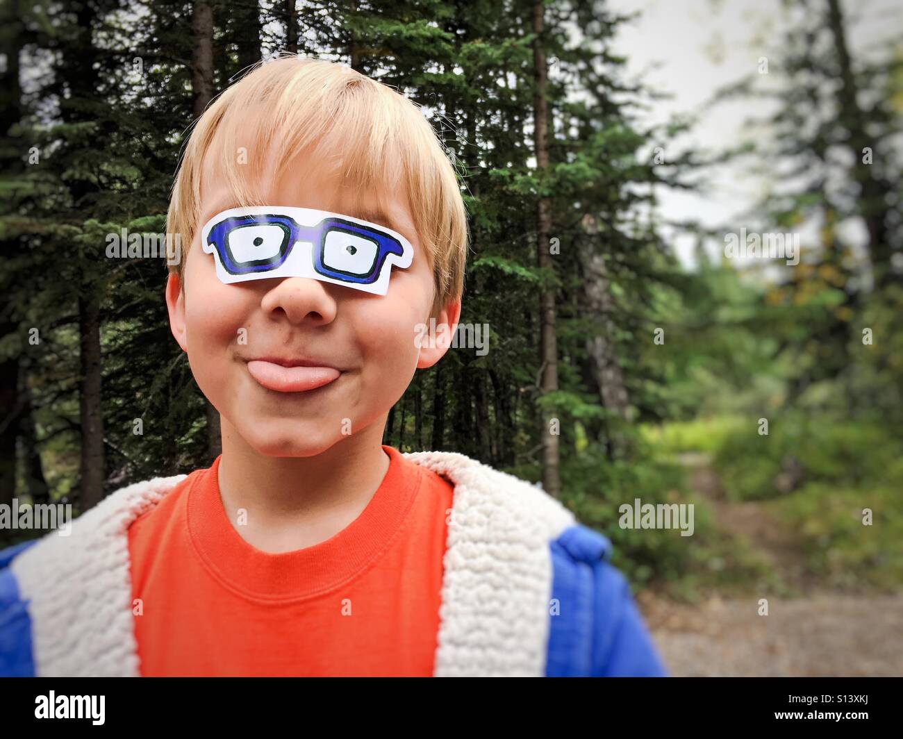 Un ragazzo bastoni fuori la sua lingua come suona con un adesivo che assomigliano a bicchieri bloccato oltre i suoi occhi. - Immagine stock catturata con smartphone