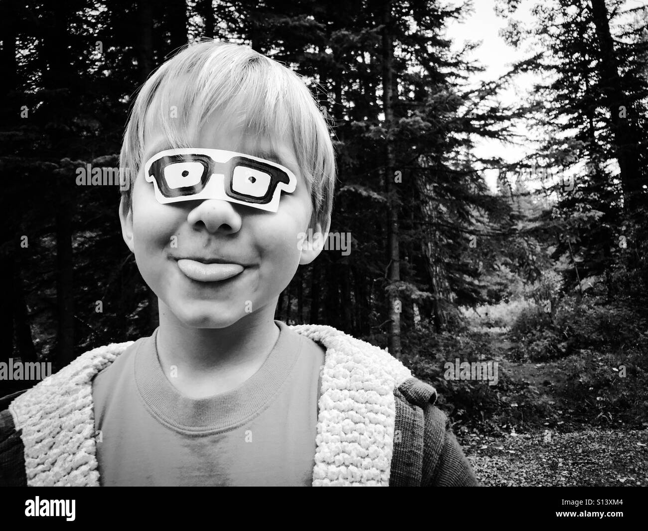 Un ragazzo bastoni fuori la sua lingua indossando un adesivo che assomigliano a bicchieri oltre i suoi occhi. Foto Stock