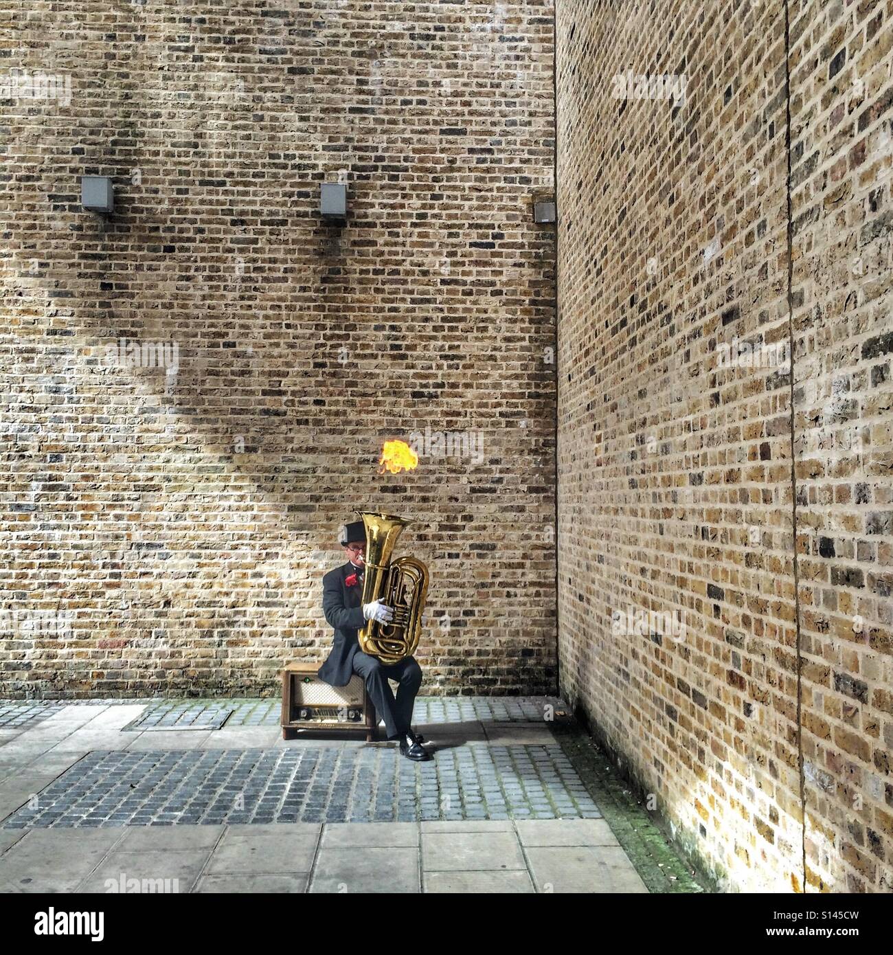 La pratica rende perfetti - un musicista di strada musicista che gioca la tuba con una fiamma soffiando fuori sopra - Immagine stock catturata con smartphone