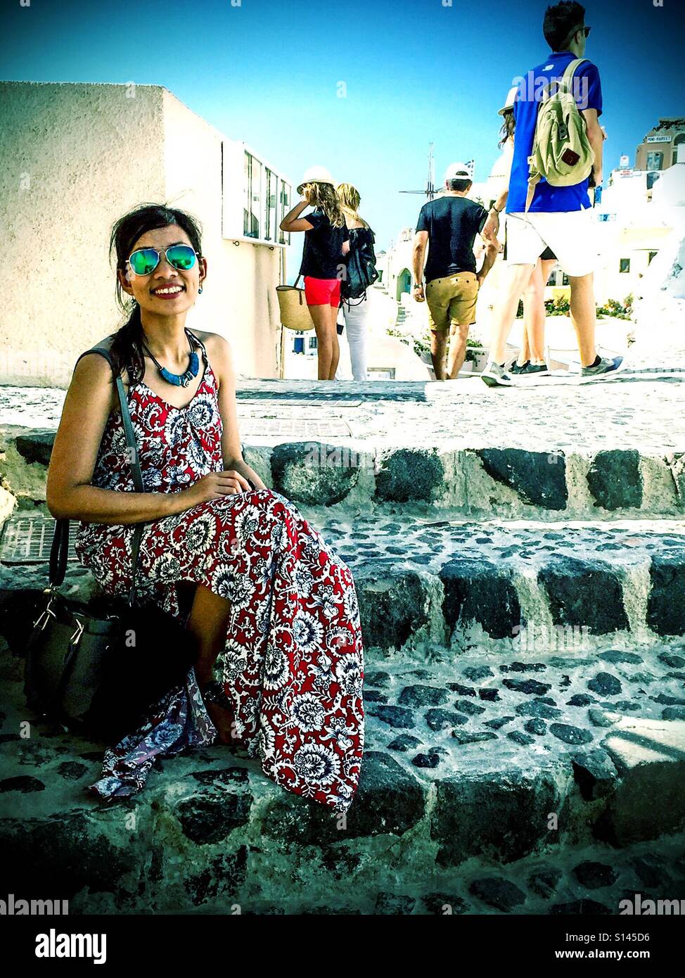 Una signora siede su alcuni passi nella cittadina di Oia sull'isola greca di Santorini. - Immagine stock catturata con smartphone