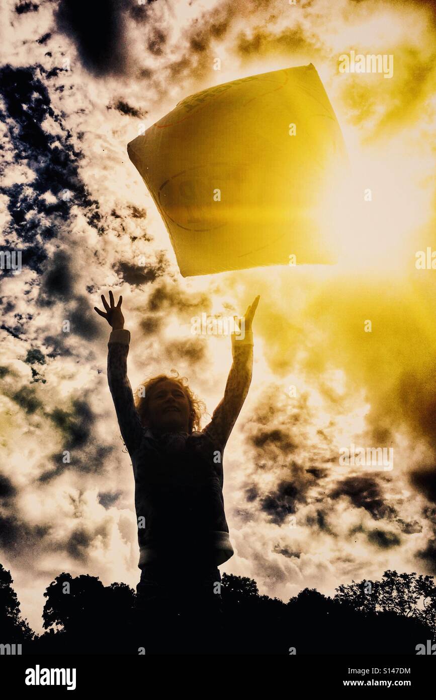 Giovane ragazza gettando gonfiabile gigante cubo in aria retroilluminati da Sun Foto Stock