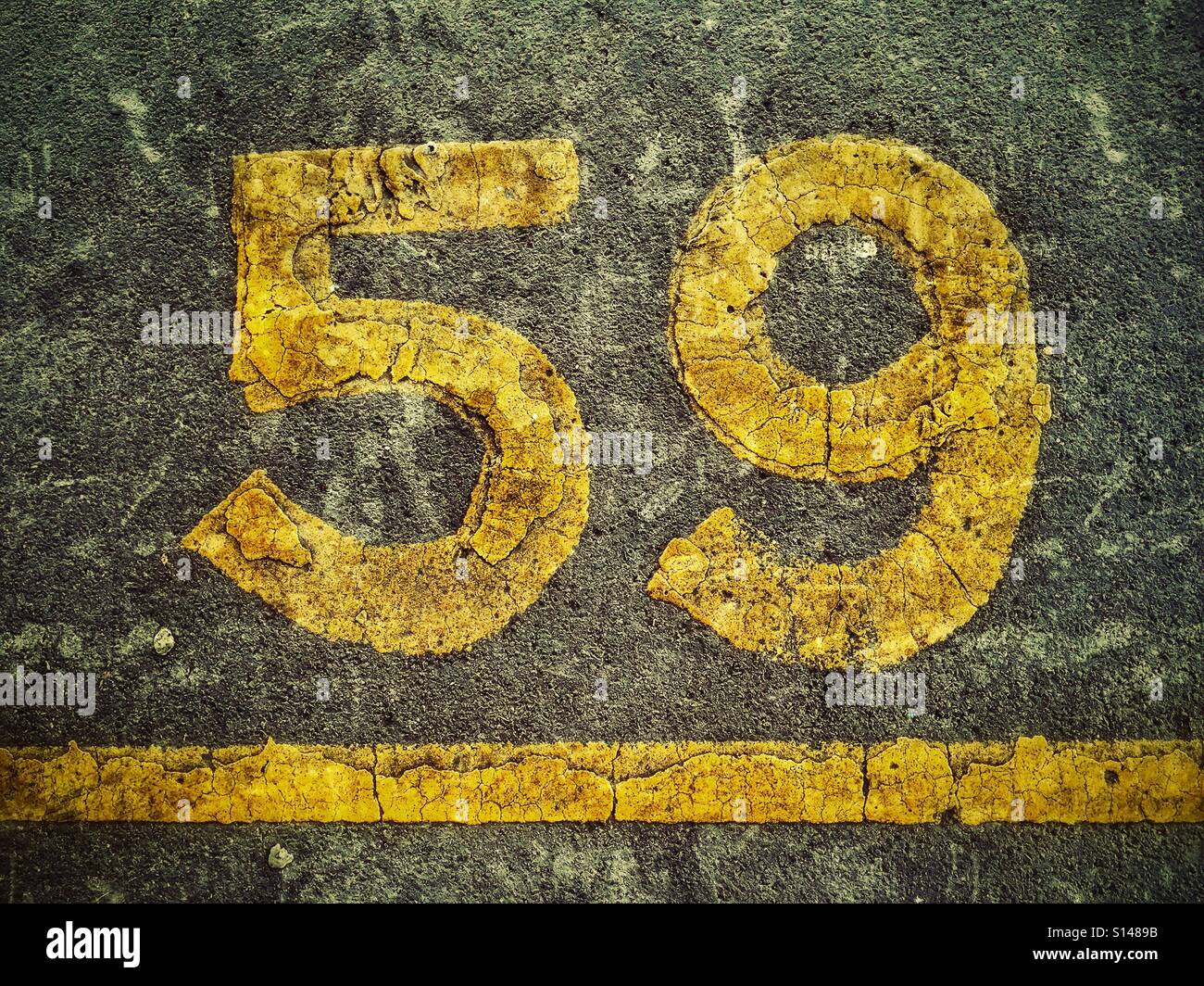 Il numero 59 scritto in vernice gialla su una superficie asfaltata. Questo è spazio parcheggio numero cinquanta nove. Credito foto - © COLIN HOSINS. - Immagine stock catturata con smartphone