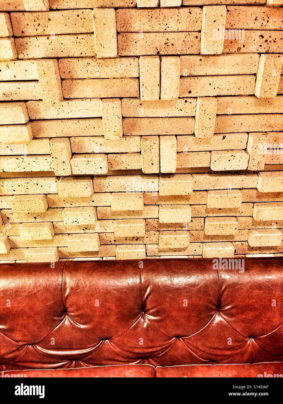 Giallo artistico di un muro di mattoni al di sopra di un divano in pelle Foto Stock