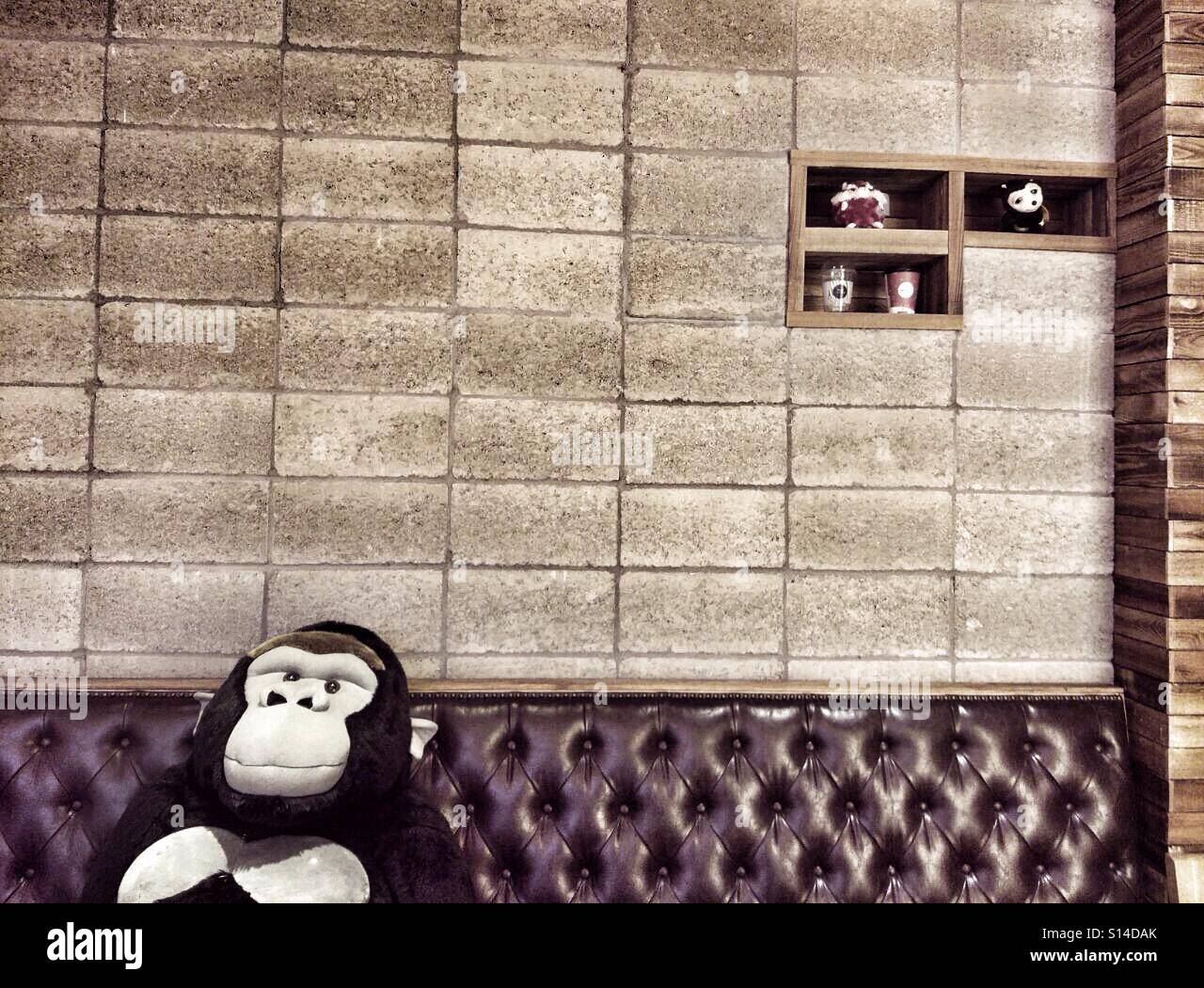 Giocattolo imbottito Gorilla si siede sul divano di pelle in un cafe in attesa per i clienti Foto Stock