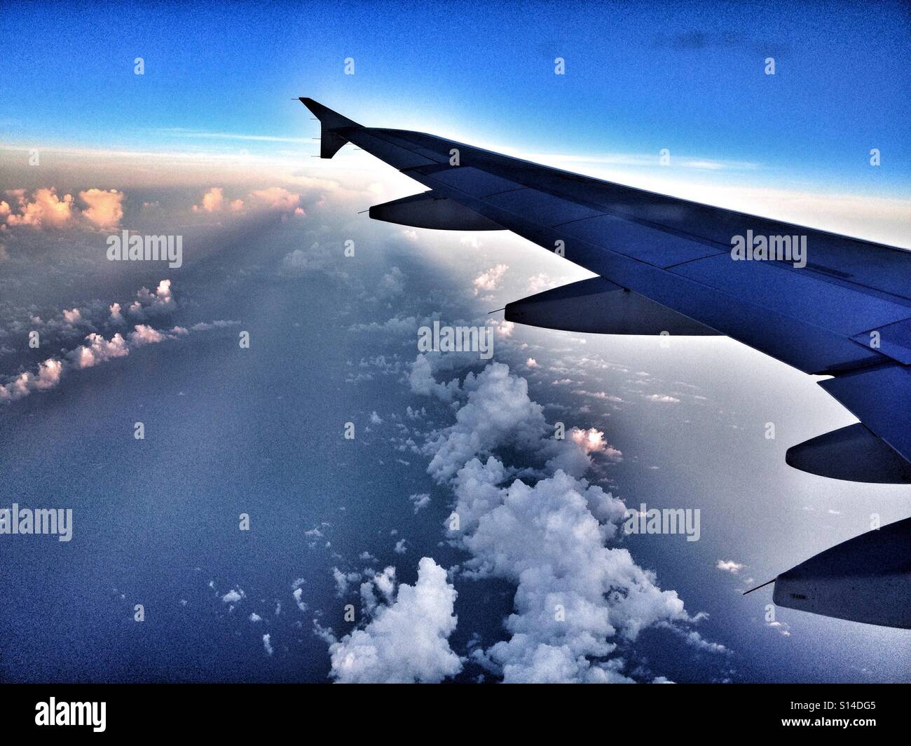 L'ala sinistra di un aereo in alto sopra le nuvole, con cielo blu Foto Stock