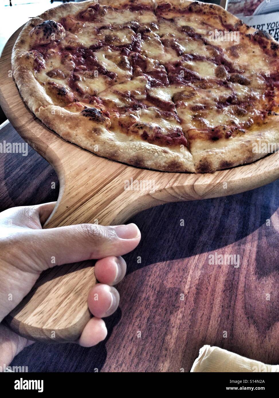 Pane appena sfornato artigianale di formaggi italiani Pizza dopo essere stato prelevato da un muro di pietra forno su una pizza in legno vassoio da forno Foto Stock