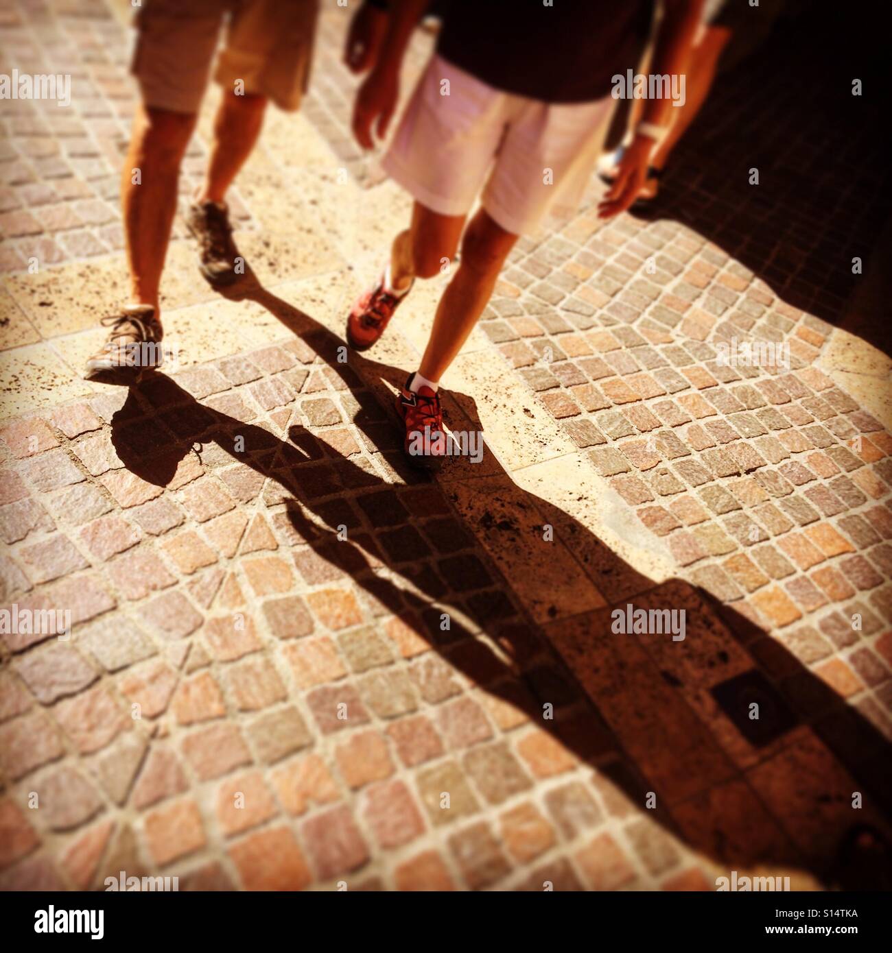 Due uomini per le gambe, sezione bassa. Camminare sotto il sole con lunghe ombre che si allunga davanti a loro. Foto Stock