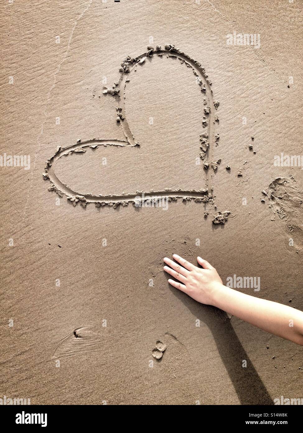 Una sola mano è una schematizzazione di un disegno di cuore nella sabbia - rappresenta un esempio di amore e romanticismo, la spiaggia di sabbia e il mare Foto Stock