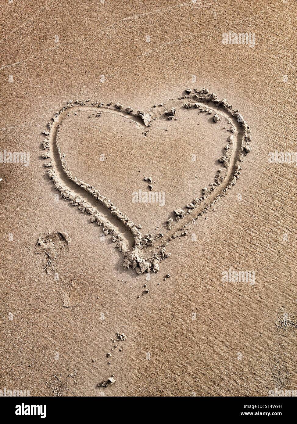 Dito di disegno a forma di cuore sulla sabbia della spiaggia Foto Stock