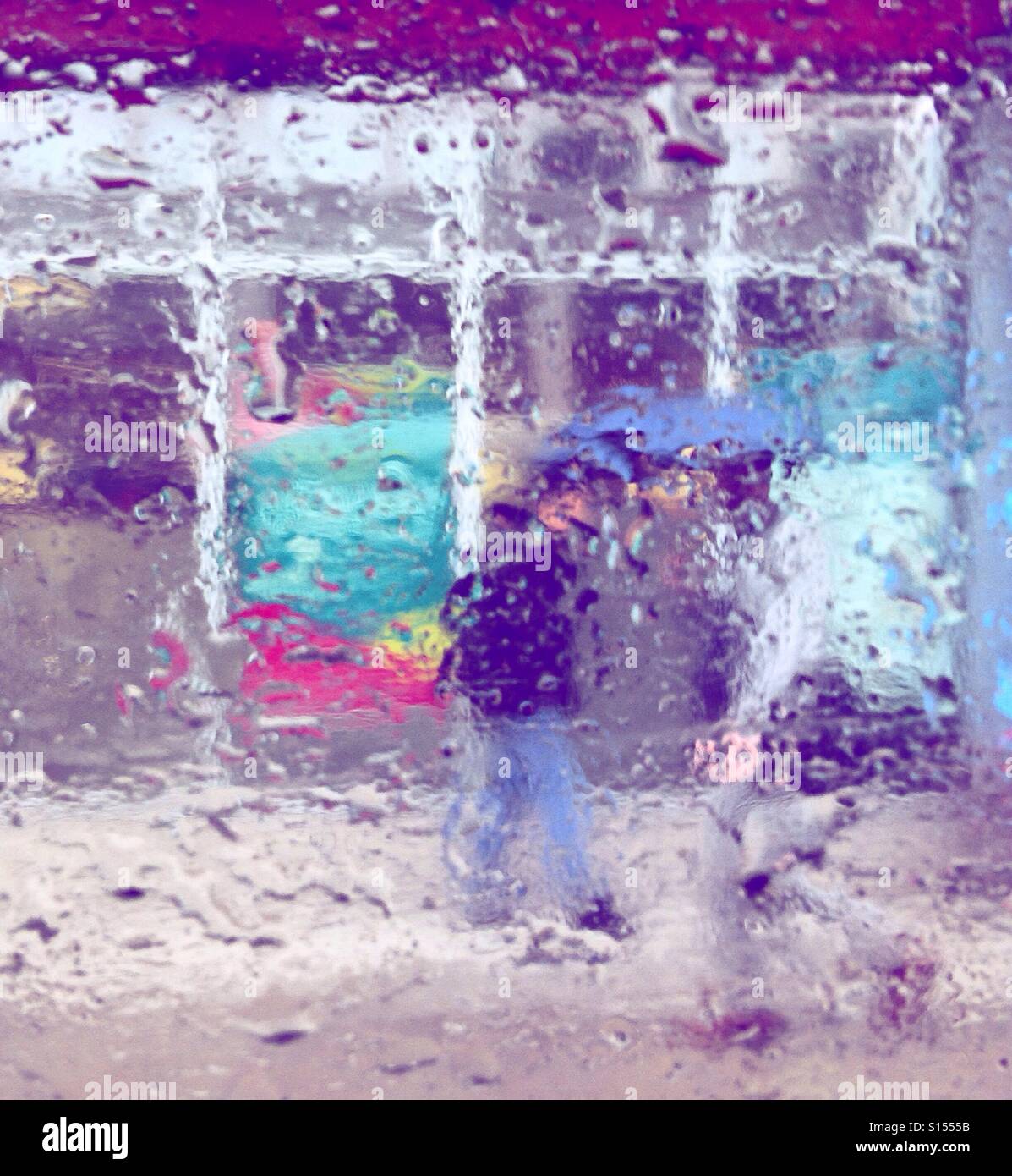 Persone con ombrelloni visibile attraverso le gocce di pioggia su una finestra Foto Stock
