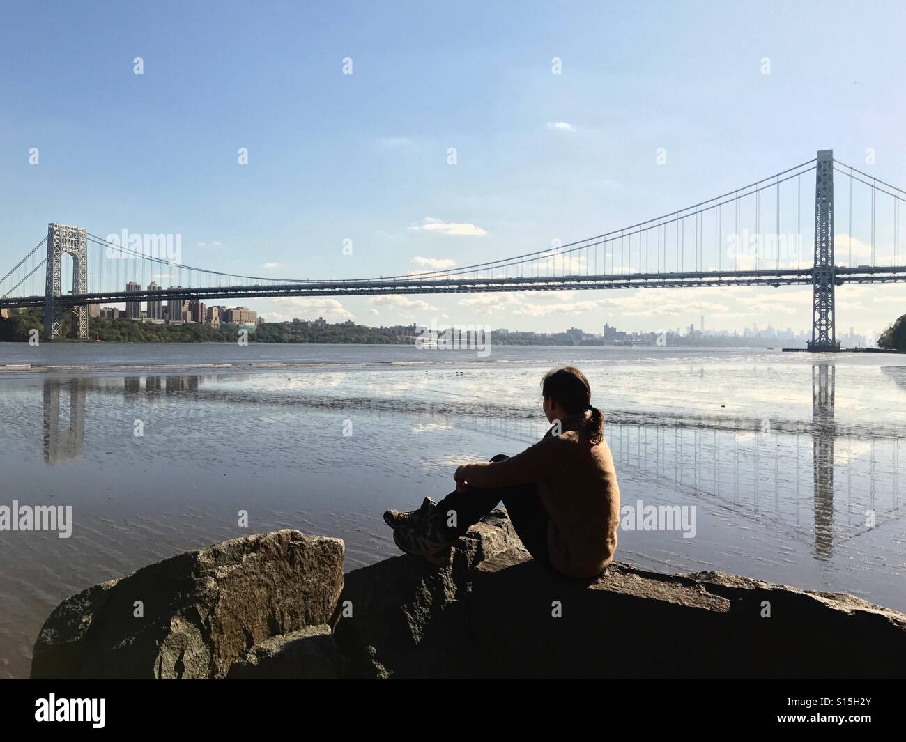 Una donna seduta dal fiume Hudson con la vista del Ponte George Washington Bridge, New Jersey, USA. Foto Stock