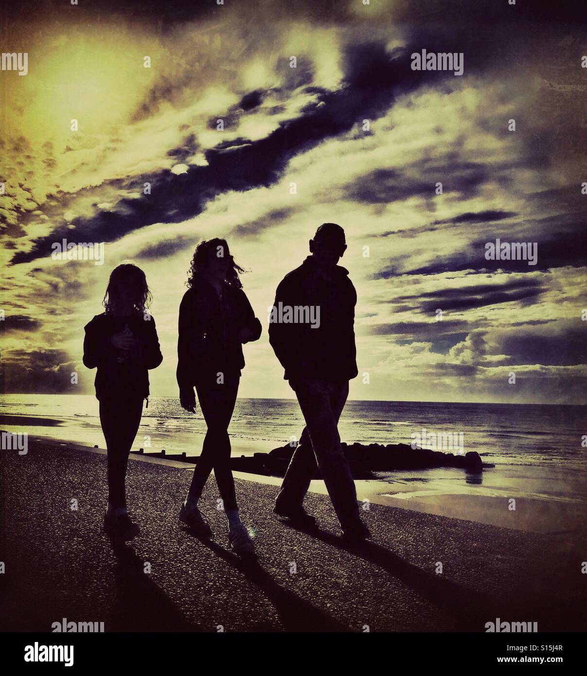 Tre persone in silhouette a piedi lungo accanto al mare (adulti e due bambini) Foto Stock