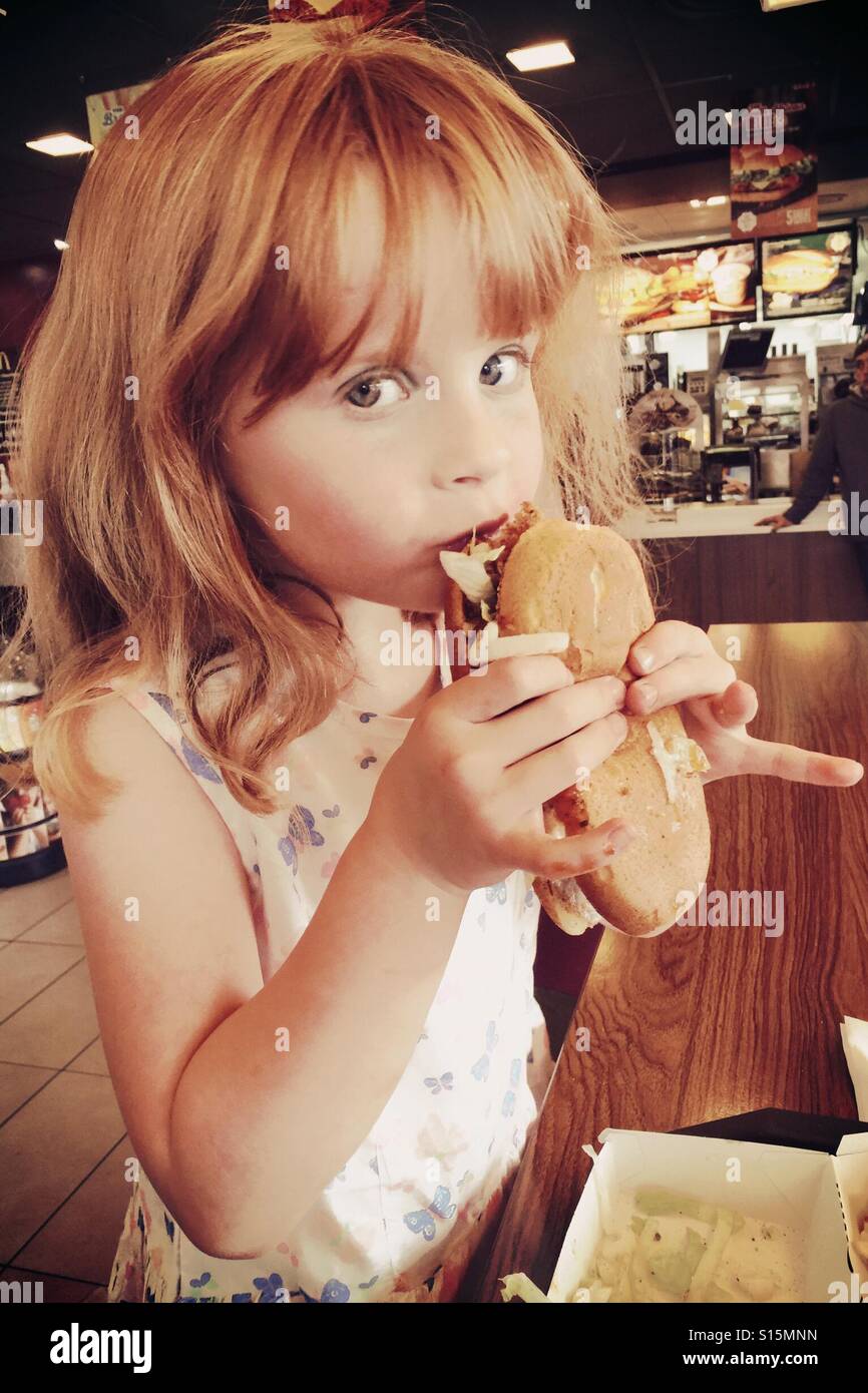 Giovani 6 anno vecchia ragazza mangiare McDonald's pollo Burger legenda nel ristorante da asporto Foto Stock