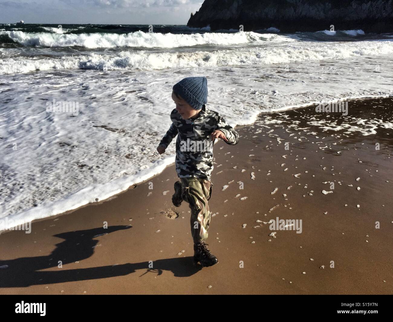Un 9 anno-vecchio ragazzo corre lontano dall'acqua di mare come una più grande di quanto ci aspettassimo wave arriva alla spiaggia di Baia Barafundle nel Galles di Ottobre 2016 Foto Stock