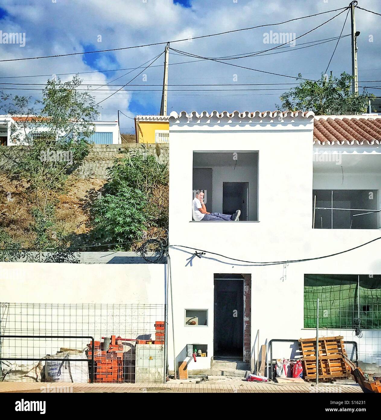 Operaio edile prendendo una pausa seduti in balcone aperto finestrino di una proprietà residenziale in costruzione in Spagna con materiali da costruzione dal ciglio della strada Foto Stock