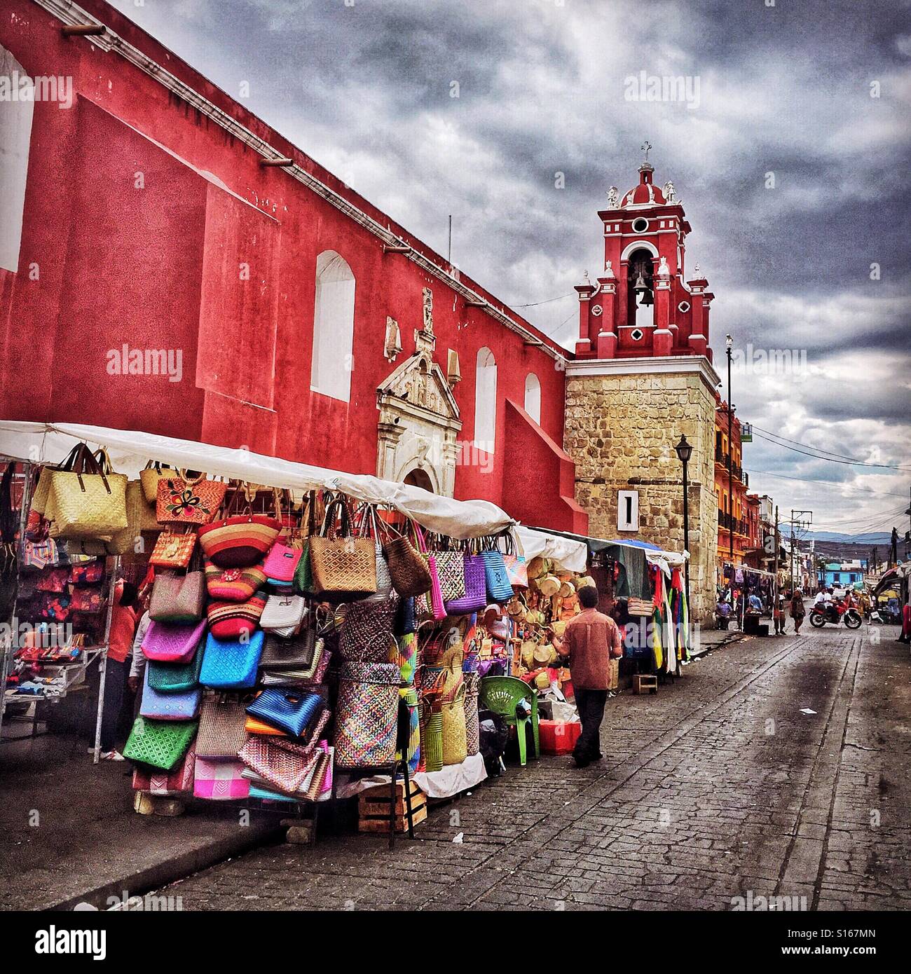 Un colorato marciapiede street market venditore in Oaxaca visualizza borse e borsette in ogni colore per catturare l'attenzione degli acquirenti. Foto Stock