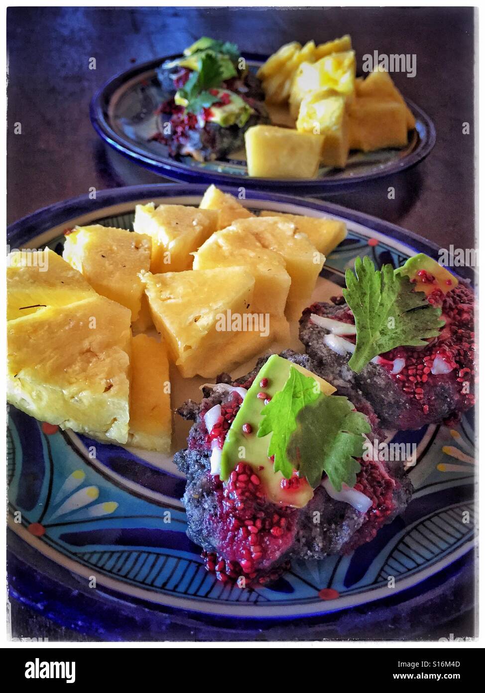 Blue masa sopes sono conditi con formaggio Oaxaca, avocado, il coriandolo, e sciroppo di hibiscus e servita con ananas fresco per un pasto delizioso. Foto Stock