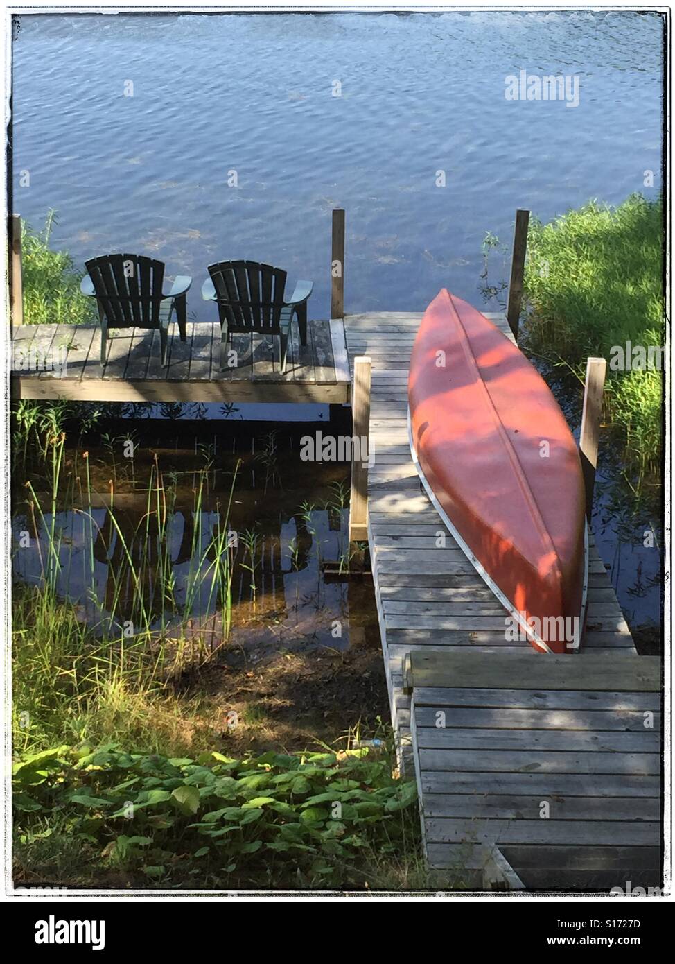 Poltrone Adirondack e canoa sul dock su un lago nel Adirondacks, New York, USA, 2015 © Katharine Andriotis Foto Stock
