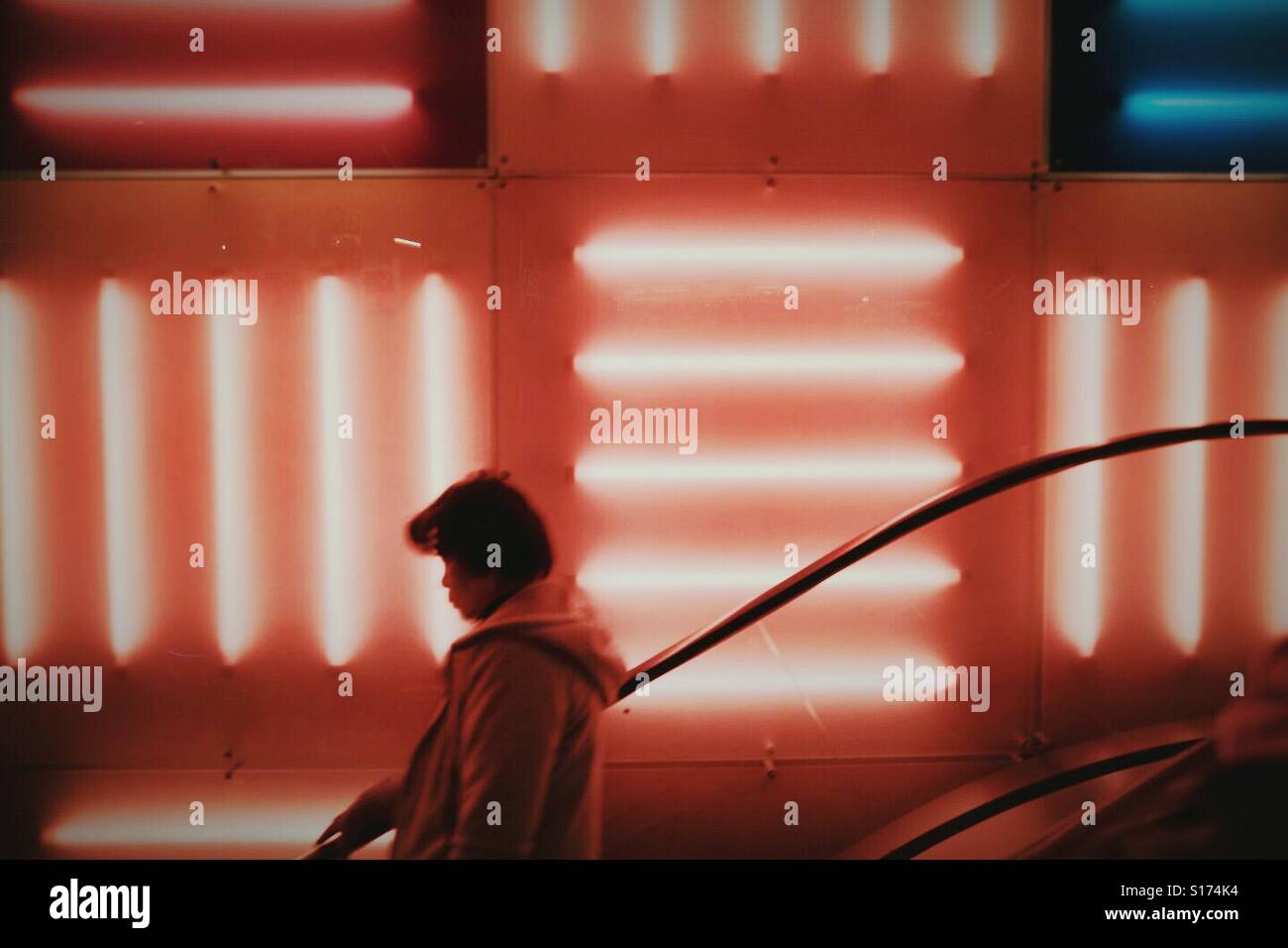 La donna in sella ad una scala mobile nella parte anteriore del rosso luci al neon Foto Stock